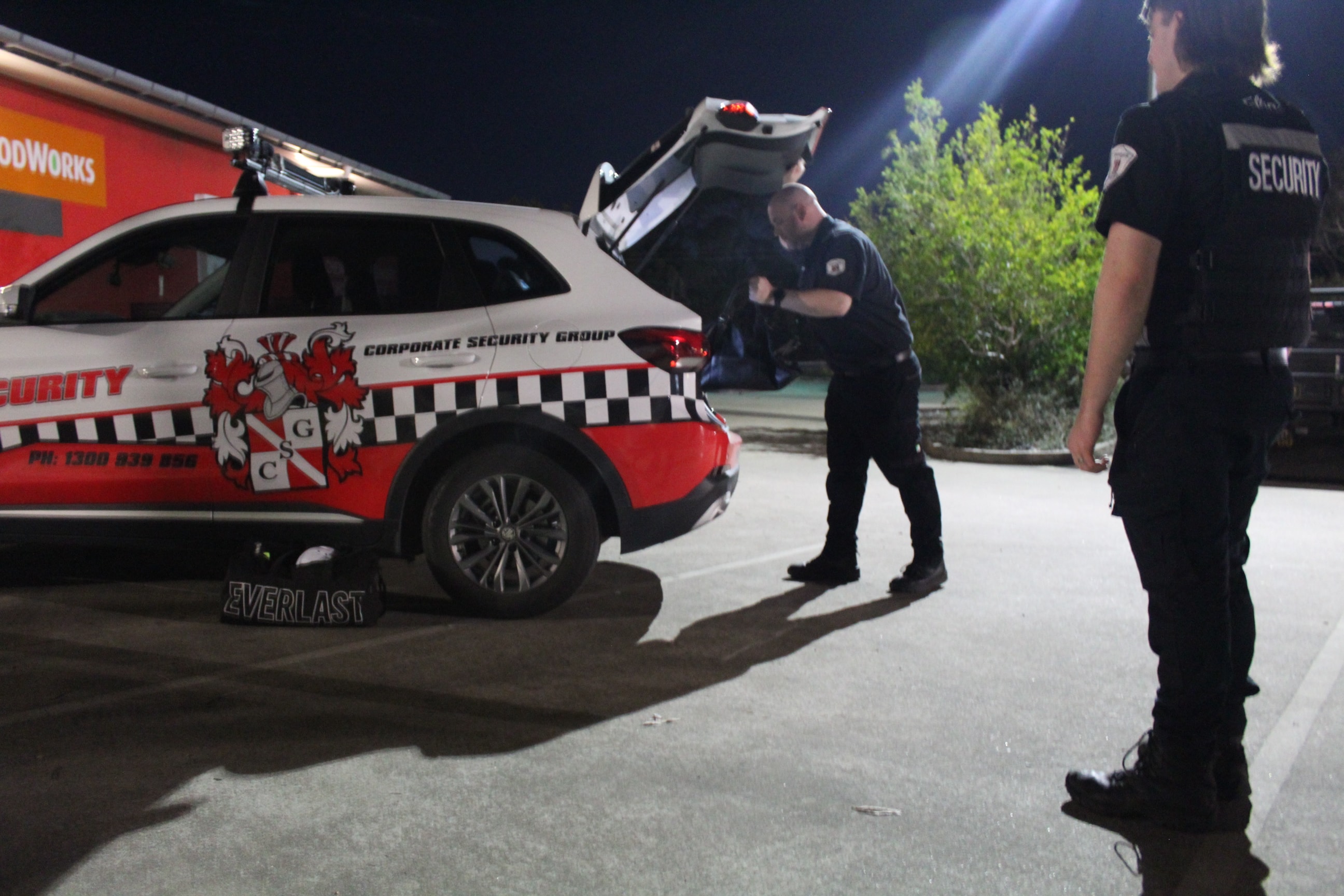 Two CSG security officers preparing equipment at the boot of a branded Corporate Security Group patrol vehicle at night