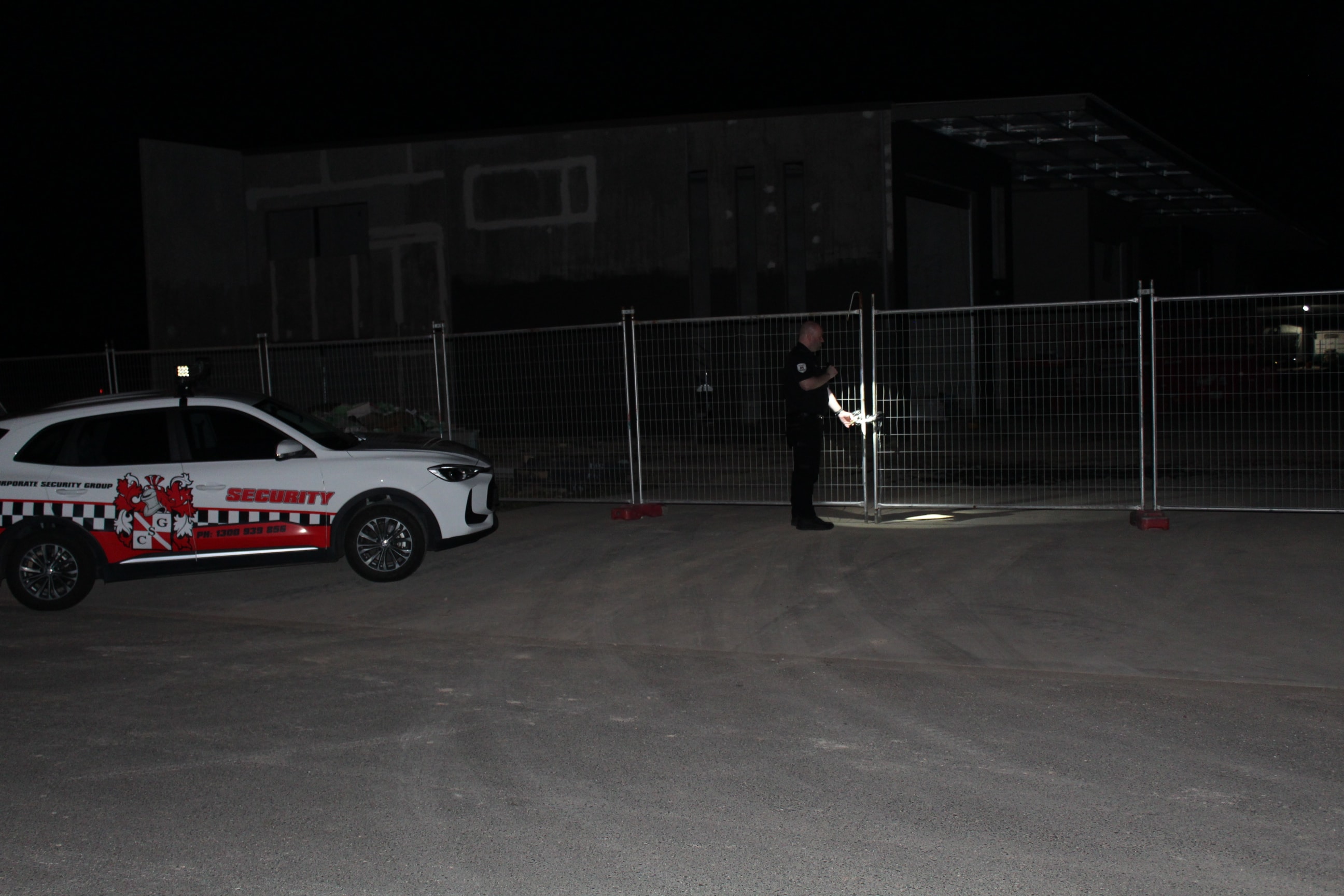 CSG officer securing a construction site gate at night beside a branded patrol vehicle