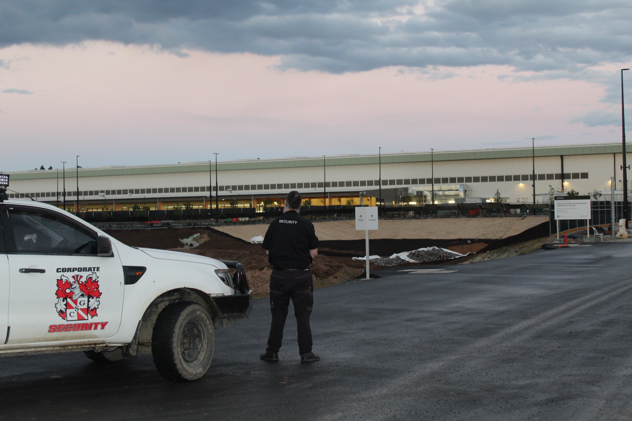 CSG security officer standing beside branded patrol vehicle monitoring a large construction site at dusk